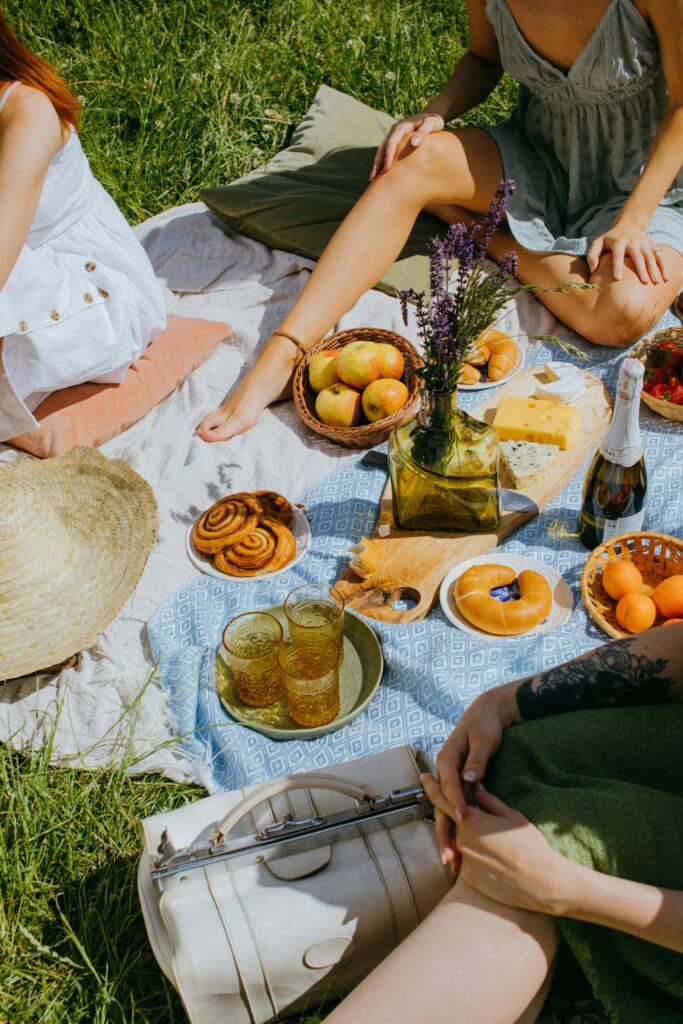 Enjoying a sunny picnic with fruits, pastries, and drinks on a lush green field.